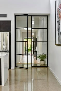 an open glass door leading to a kitchen and living room with white walls, marble flooring and large painting on the wall