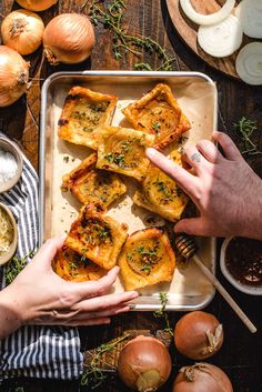 two hands reaching for some food on a tray with onions and garlic next to it