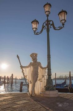 a statue is standing next to a lamp post on the water with boats in the background