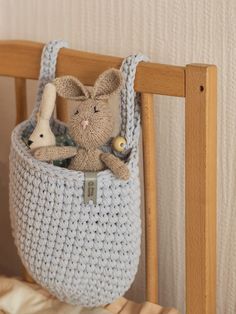 a crocheted basket with a stuffed animal in it sitting on a wooden chair