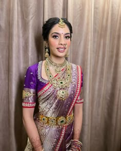 a woman in a purple and gold bridal outfit standing next to a brown curtain