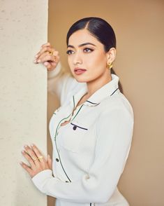 a woman in white shirt and gold ring leaning against wall with her hand on the corner