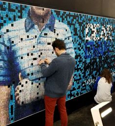 two people working on an art piece in front of a wall covered with squares and pixels