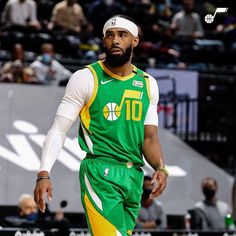 a basketball player in green and yellow uniform walking on the court with his foot up