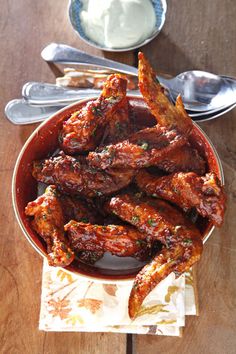 a bowl filled with wings covered in sauce next to spoons and utensils