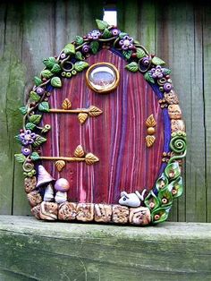 a fairy door with purple and green decorations on it's side, in front of a wooden fence