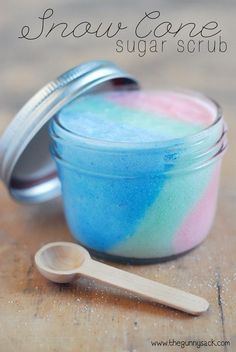 a jar filled with blue and pink sugar next to a spoon on top of a wooden table