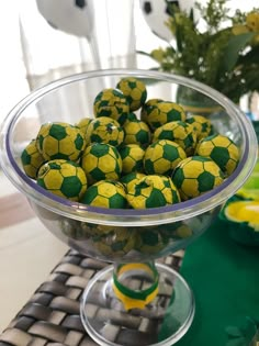 a bowl filled with yellow and green soccer balls on top of a table next to flowers