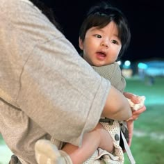 a woman holding a small child in her arms while standing next to a park at night