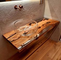 a glass bowl sitting on top of a wooden table next to a sink and faucet