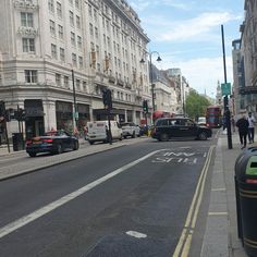 a busy city street with cars and people walking on the side walk, in front of tall buildings