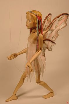 a wooden doll holding two strings attached to it's body and wearing a fairy costume