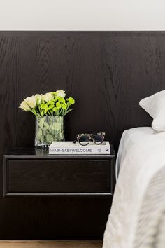 a nightstand with a book and sunglasses on it next to a flower vase filled with flowers