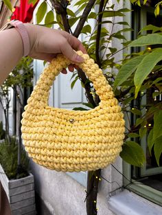 a hand holding a yellow purse next to a tree