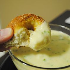 a hand holding a doughnut over a glass filled with cream cheese and broccoli