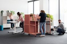 three people working in an office setting with desks, chairs and plant boxes on wheels