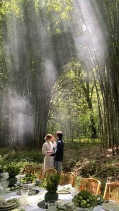 a man and woman standing in front of a bamboo forest with mist coming from the trees