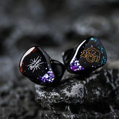 pair of ear buds with colorful designs on them sitting on rock next to black background