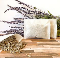 two bags with dried herbs next to them on a wooden table, one bag is white and the other has purple flowers in it