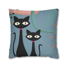 two black cats sitting on top of a blue pillow with pink and green circles in the background