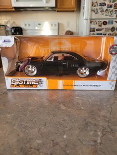 a black toy car in a box on a kitchen counter