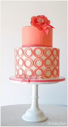 a three tiered cake with pink icing and a flower on top, sitting on a white pedestal