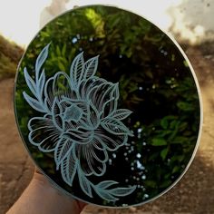 a hand holding a glass plate with a flower etched on the front and back side