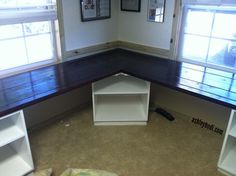 an empty room with two windows and a book shelf on the floor in front of it