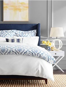 a bed with blue and white comforter in a bedroom next to a painting on the wall