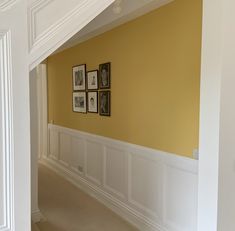 an empty hallway with pictures on the wall and white wainscoting around it