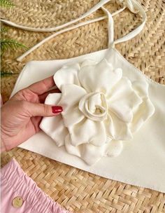 a woman's hand holding a flower on top of a piece of cloth next to a straw hat