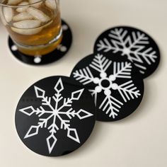 three coasters with snowflakes on them next to a glass filled with ice