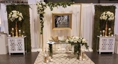 a white and gold wedding set up with flowers, candles and greenery on the stage