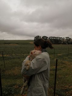 a woman holding a dog in her arms while standing on a lush green field under a cloudy sky