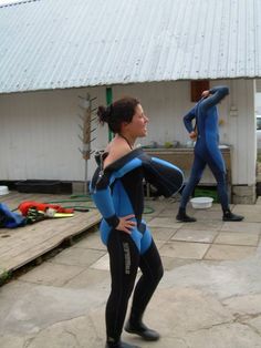 two women in wetsuits are standing outside