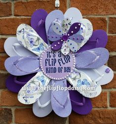 a purple and white flip flop wreath hanging on a brick wall with the words it's a flip flop day