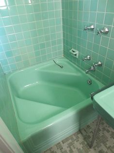 a green bath tub sitting next to a white sink in a bathroom with tiled walls