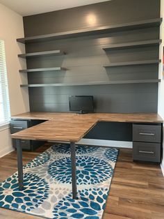 a room with a desk, shelves and a rug on the floor in front of it