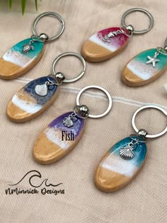 six different colored wooden key chains with charms attached to them on a beige fabric background