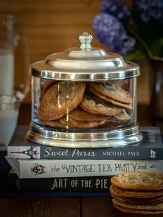 a stack of books sitting on top of a table next to a glass jar filled with cookies