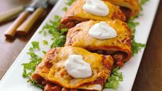 three enchiladas on a white plate with sour cream