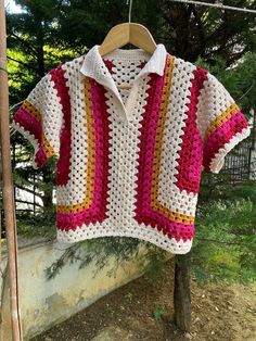 a crocheted shirt hanging on a clothesline in front of a tree and fence