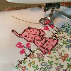 the sewing machine is stitching an elephant design on a piece of white fabric with pink and blue flowers