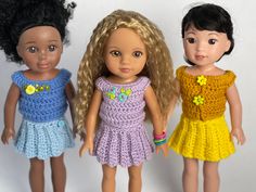 three dolls standing next to each other in front of a white background and one is wearing a crocheted dress