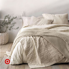 a bed with white linens and pillows in a room next to a potted plant