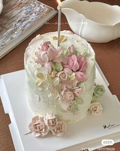 a white cake with pink flowers on it and a single lit candle in the middle