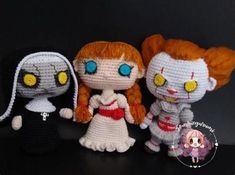 three crocheted dolls sitting next to each other on a black surface with one doll wearing a white dress