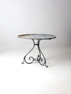 an iron table with a glass top on a white background in front of a wall