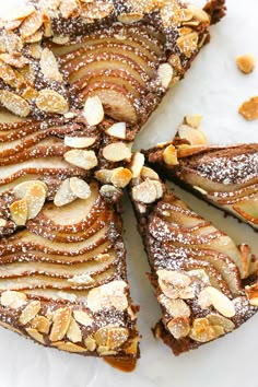 a sliced cake with almonds and powdered sugar on top, sitting on a white surface