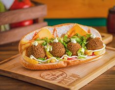 a sandwich with meatballs, lettuce and cheese on it sitting on a cutting board